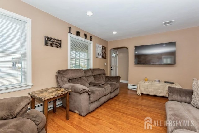 living area with visible vents, arched walkways, light wood-style floors, baseboard heating, and a healthy amount of sunlight