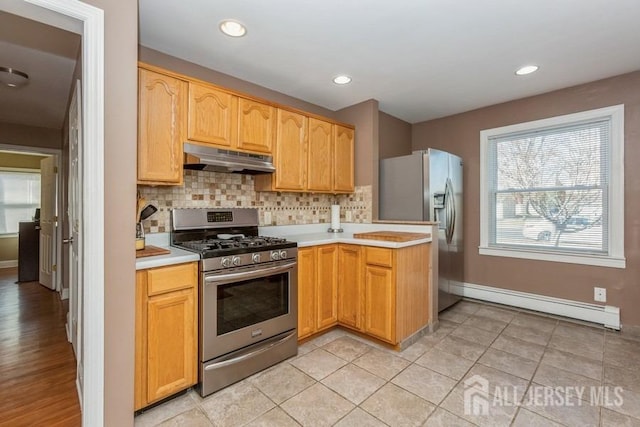 kitchen with light countertops, a baseboard radiator, under cabinet range hood, and stainless steel appliances