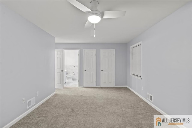 unfurnished bedroom featuring ceiling fan, light colored carpet, two closets, and ensuite bath