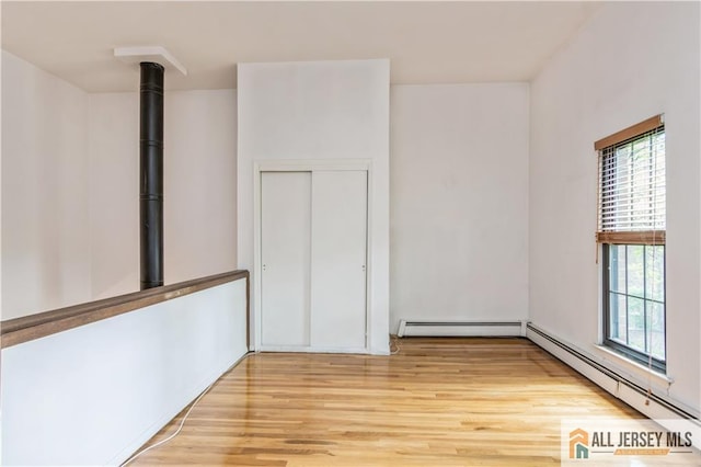 323 Gills Ln Unit 9C, Iselin, NJ 08830 - empty room with healthy amount of natural light, light wood finished floors, and a baseboard heating unit