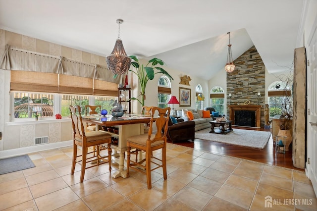 dining room featuring a healthy amount of sunlight, a stone fireplace, lofted ceiling, and light tile patterned flooring