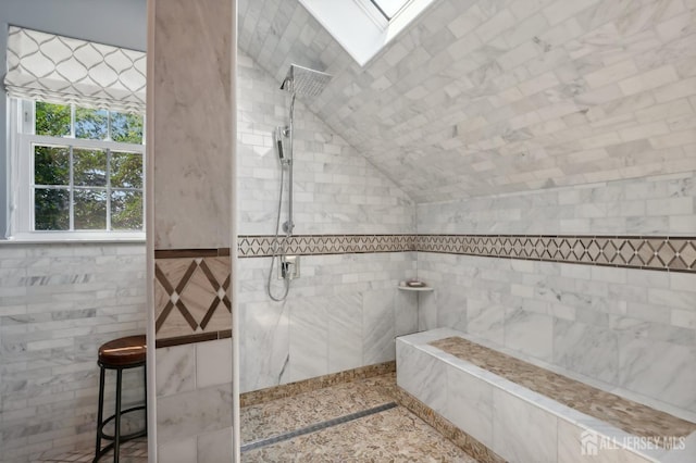 bathroom featuring a tile shower, tile walls, and vaulted ceiling with skylight