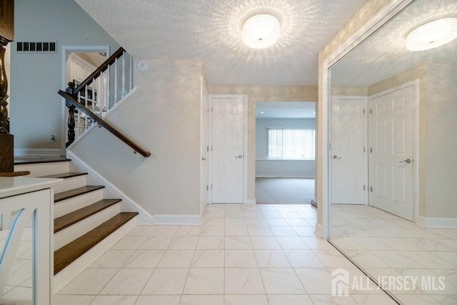 foyer entrance with baseboards, stairs, visible vents, and a textured ceiling