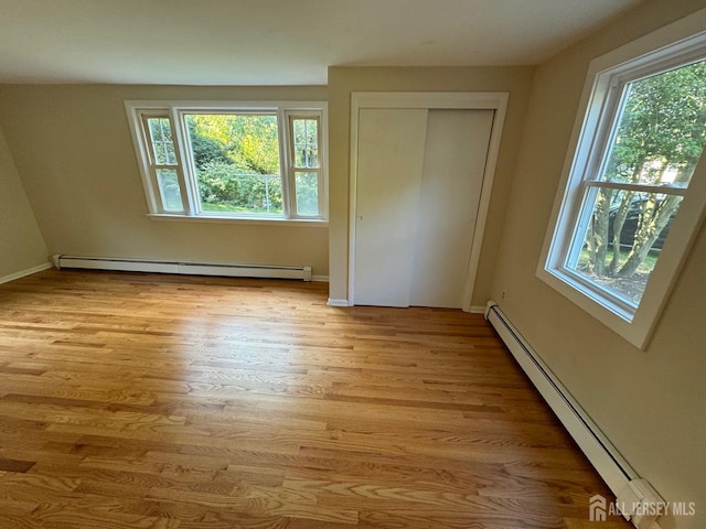 unfurnished bedroom featuring a closet, a baseboard heating unit, and light wood-type flooring