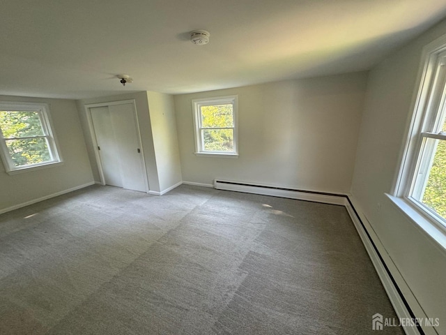 empty room featuring a baseboard heating unit, light colored carpet, and plenty of natural light