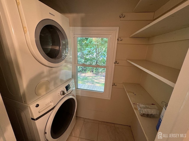 clothes washing area with stacked washer / drying machine and light tile patterned floors