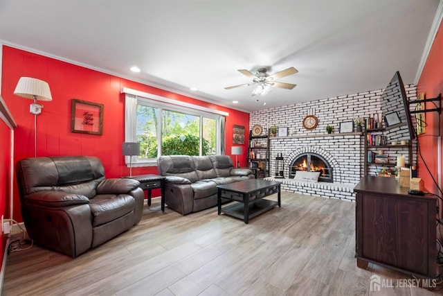 living room featuring ceiling fan, wood finished floors, a fireplace, brick wall, and an accent wall