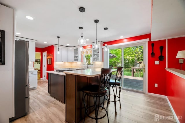 kitchen with freestanding refrigerator, light countertops, white cabinets, a sink, and gas cooktop