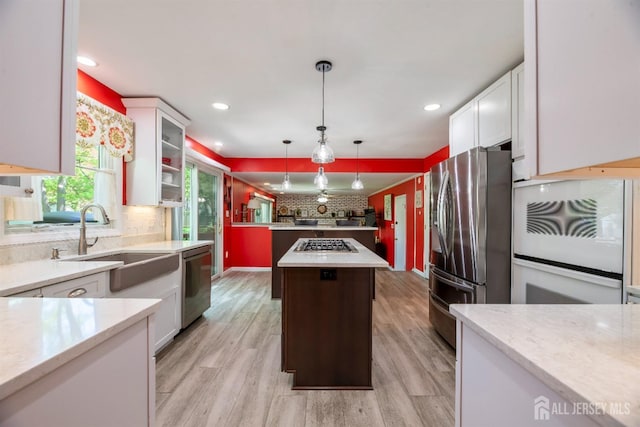 kitchen featuring appliances with stainless steel finishes, a sink, decorative backsplash, a kitchen island, and white cabinets