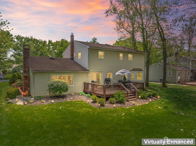 back of property at dusk featuring a chimney, a deck, and a lawn