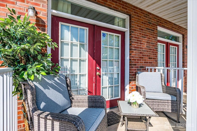 entrance to property with brick siding, a porch, and french doors