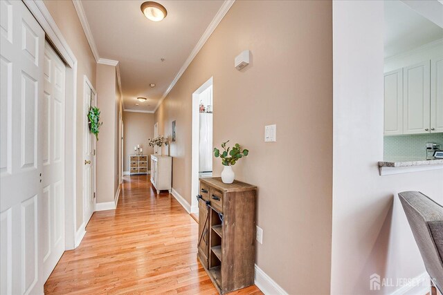 hallway with crown molding, light wood-style floors, and baseboards