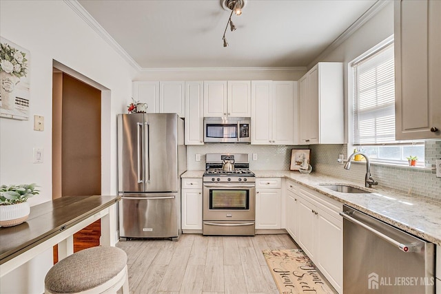 kitchen featuring stainless steel appliances, a sink, light stone countertops, white cabinetry, and ornamental molding