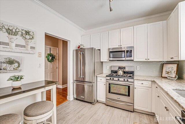 kitchen featuring appliances with stainless steel finishes, ornamental molding, white cabinetry, decorative backsplash, and light stone countertops
