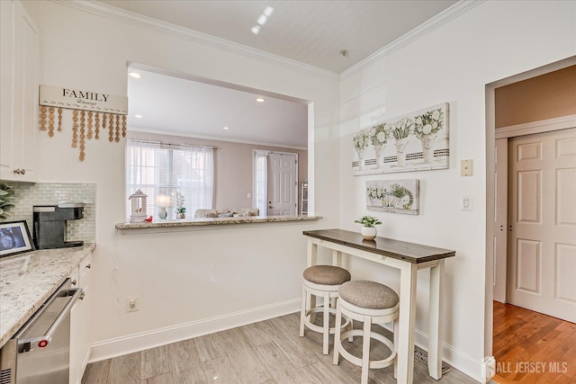 kitchen with stainless steel dishwasher, light wood-style flooring, baseboards, crown molding, and light stone countertops
