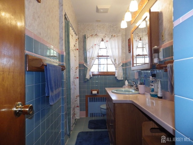 bathroom featuring radiator, toilet, tile patterned flooring, vanity, and tile walls