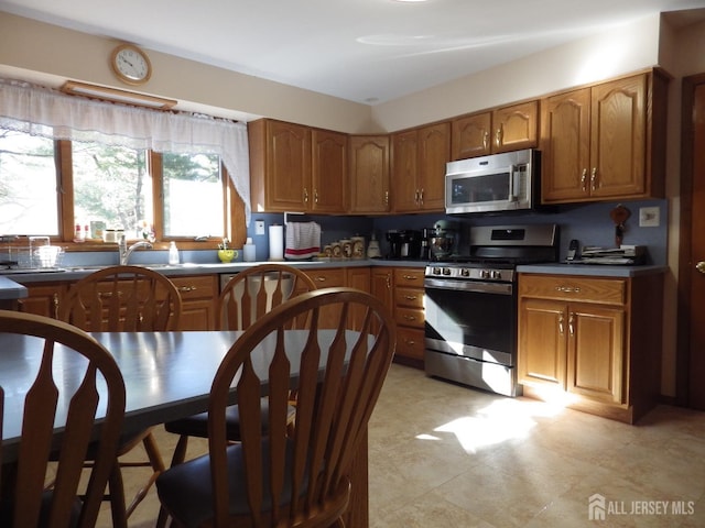 kitchen with stainless steel appliances, dark countertops, a sink, and brown cabinets