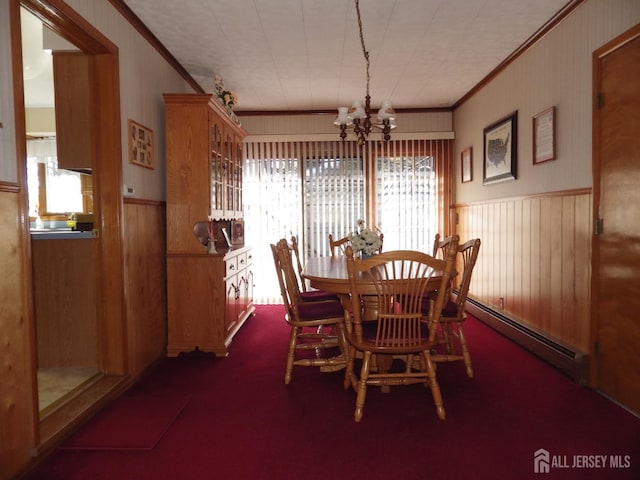 carpeted dining room with an inviting chandelier, a baseboard heating unit, crown molding, and wainscoting