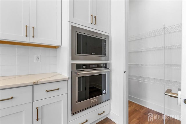 kitchen with backsplash, appliances with stainless steel finishes, dark wood finished floors, light stone counters, and white cabinets