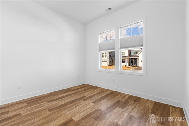 unfurnished room with wood finished floors, visible vents, and baseboards