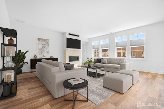 living room featuring light wood-style floors, baseboards, a glass covered fireplace, and visible vents