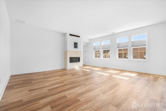 unfurnished living room with light wood-type flooring, baseboards, visible vents, and a glass covered fireplace