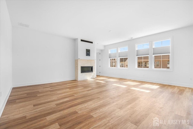 unfurnished living room featuring visible vents, baseboards, a glass covered fireplace, and light wood finished floors