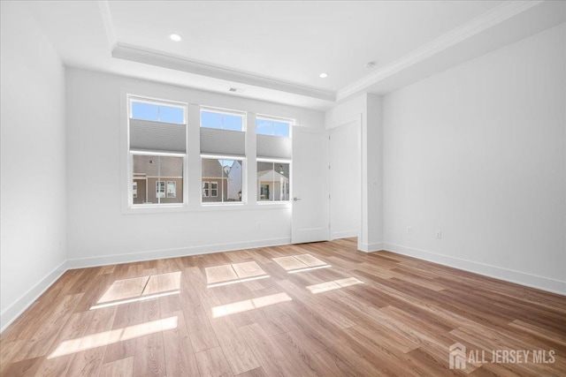 spare room with crown molding, a tray ceiling, baseboards, and light wood-style flooring