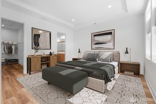 bedroom with a tray ceiling, light wood-type flooring, baseboards, and a walk in closet