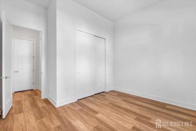 unfurnished bedroom with a closet, light wood-style flooring, and baseboards