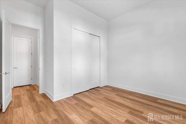 unfurnished bedroom with a closet, baseboards, and light wood-type flooring