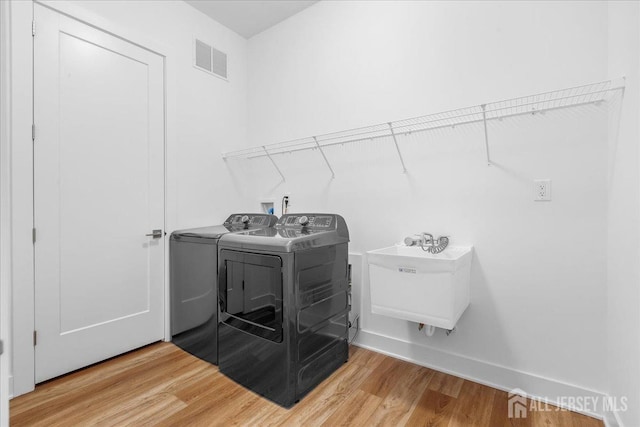 clothes washing area with washing machine and clothes dryer, laundry area, a sink, light wood-style flooring, and visible vents