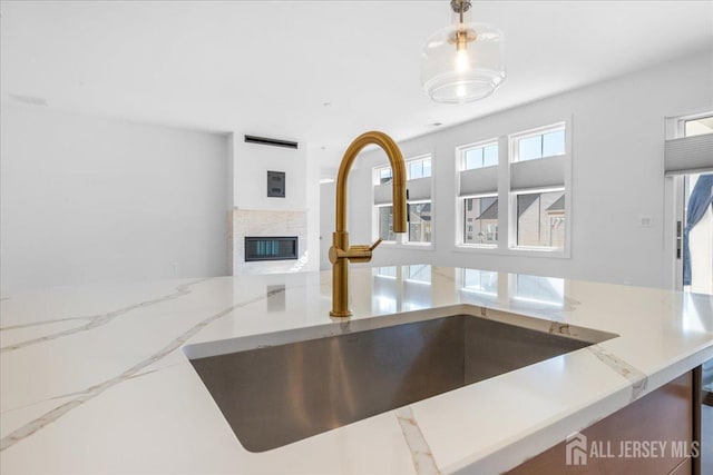 interior details featuring hanging light fixtures, light stone countertops, a glass covered fireplace, and a sink