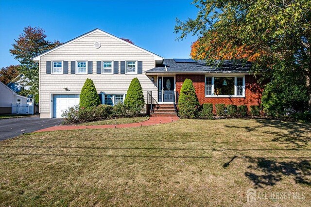 split level home with a garage, a front yard, and solar panels