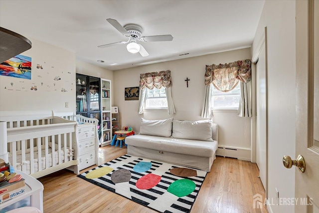 bedroom featuring a baseboard heating unit, light hardwood / wood-style floors, and ceiling fan