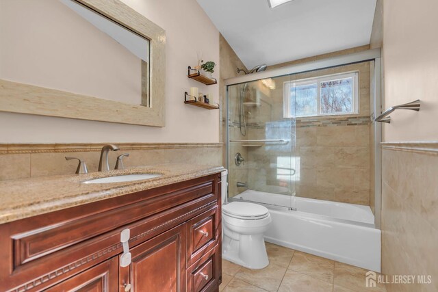 full bathroom with toilet, tile walls, vanity, enclosed tub / shower combo, and tile patterned flooring