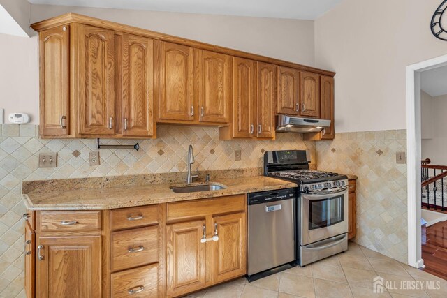 kitchen with lofted ceiling, sink, stainless steel appliances, light stone countertops, and light tile patterned flooring