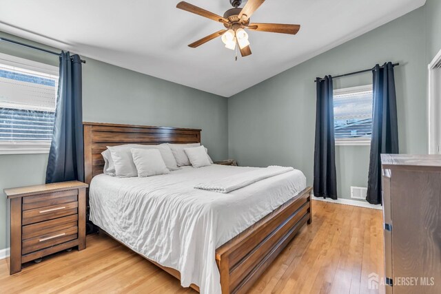 bedroom with lofted ceiling, multiple windows, light hardwood / wood-style floors, and ceiling fan