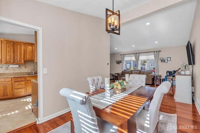 dining space featuring lofted ceiling, a notable chandelier, sink, and light wood-type flooring