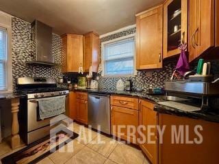 kitchen with plenty of natural light, light tile patterned floors, stainless steel appliances, and wall chimney exhaust hood