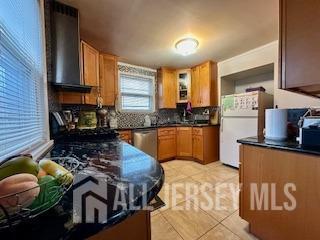 kitchen with wall chimney exhaust hood, white refrigerator, stainless steel dishwasher, and light tile patterned flooring