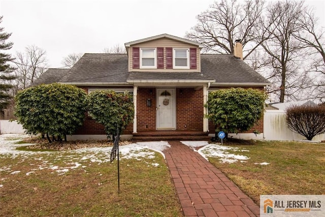 view of front of house featuring a front yard, fence, roof with shingles, a chimney, and brick siding