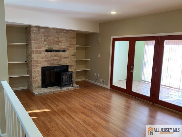 unfurnished living room featuring hardwood / wood-style flooring, french doors, built in features, and a wood stove