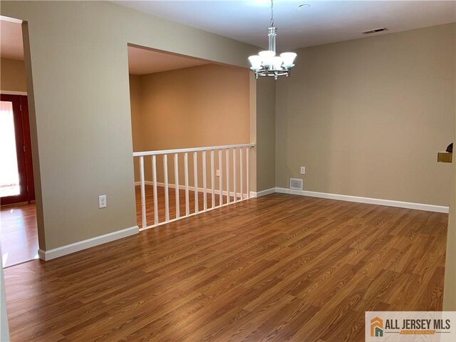 spare room with an inviting chandelier and wood-type flooring