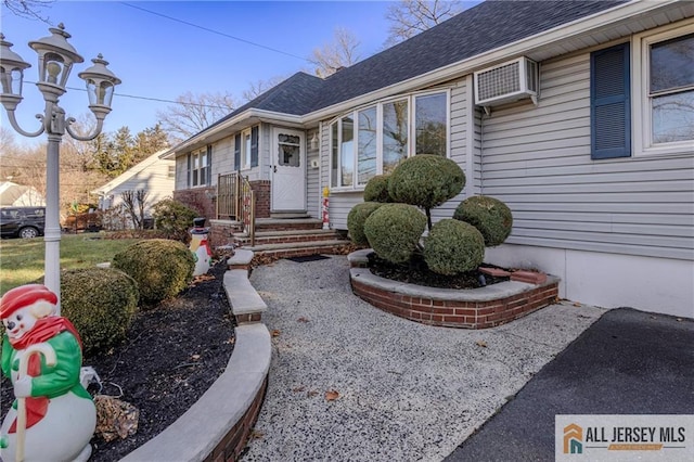 entrance to property featuring roof with shingles and a wall unit AC