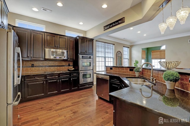 kitchen with appliances with stainless steel finishes, a sink, light wood finished floors, dark brown cabinets, and crown molding