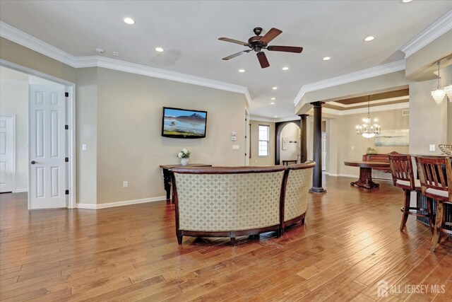 living room featuring decorative columns, a chandelier, ceiling fan, wood finished floors, and ornamental molding