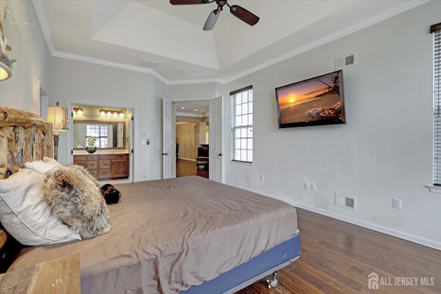 bedroom with dark wood finished floors, a raised ceiling, baseboards, ornamental molding, and ensuite bath