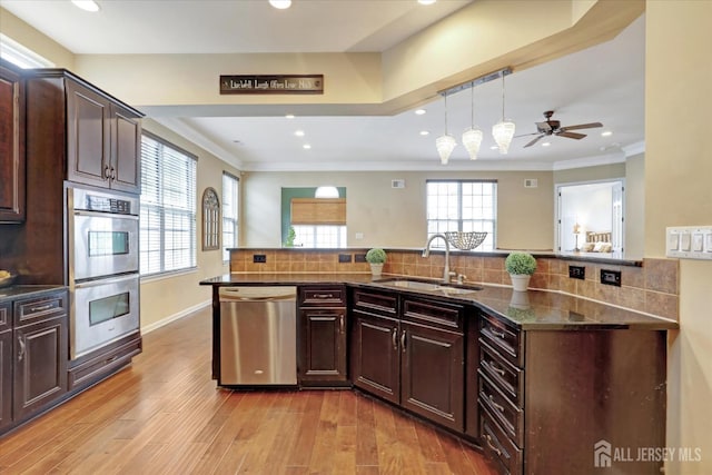 kitchen featuring appliances with stainless steel finishes, a sink, light wood finished floors, ceiling fan, and backsplash