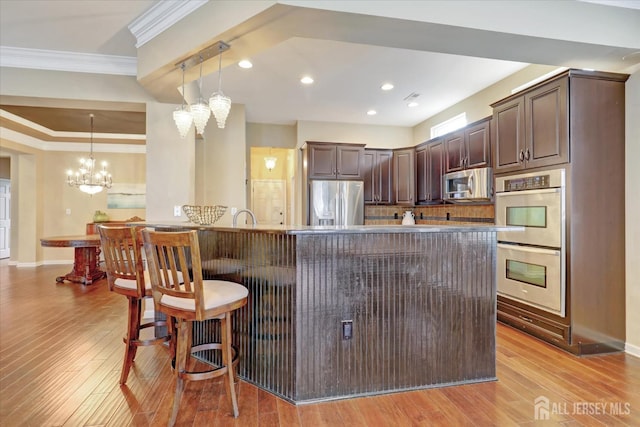 kitchen with stainless steel appliances, a chandelier, crown molding, dark brown cabinets, and a kitchen breakfast bar